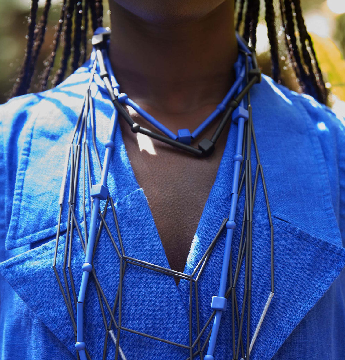 Close-up of a model wearing a blue linen shirt adorned with a geometric blue and black necklace