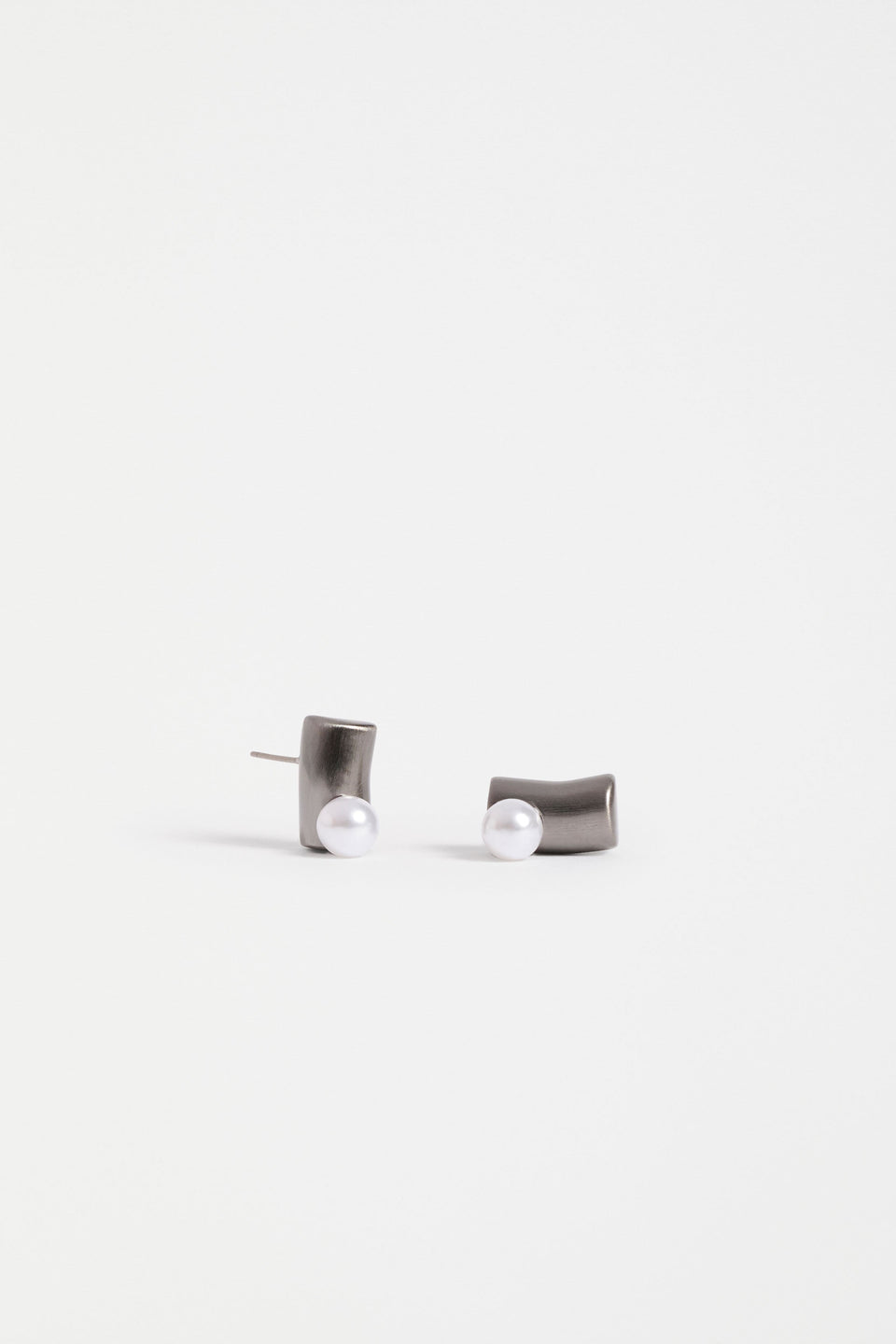 The Ahas Stud Earring features a sculptural curved form with a bold cylindrical base and delicate pearl bead accent | GUNMETAL