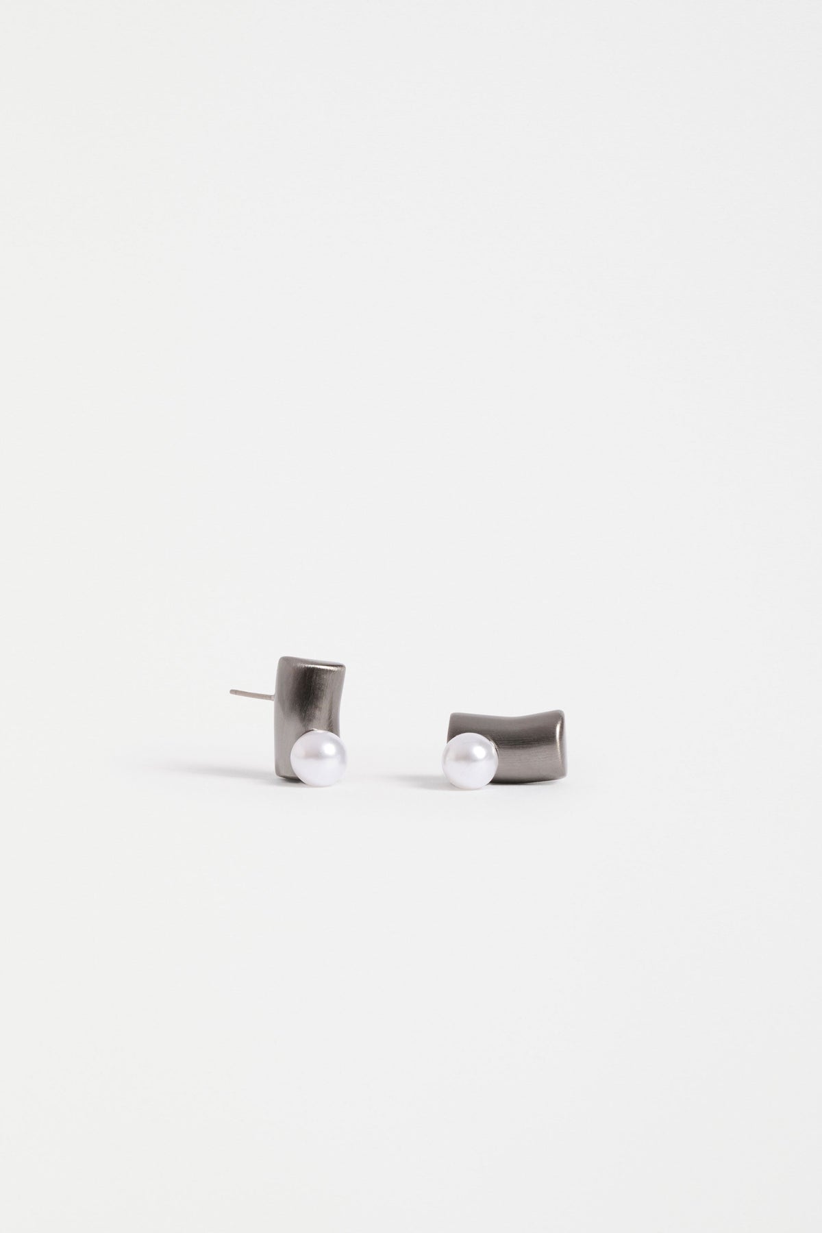 The Ahas Stud Earring features a sculptural curved form with a bold cylindrical base and delicate pearl bead accent | GUNMETAL