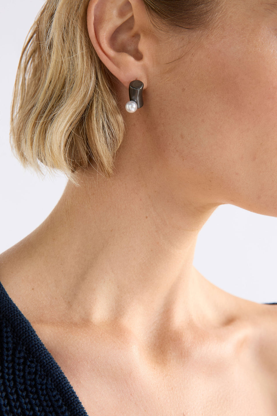 The Ahas Stud Earring features a sculptural curved form with a bold cylindrical base and delicate pearl bead accent shown on model | GUNMETAL