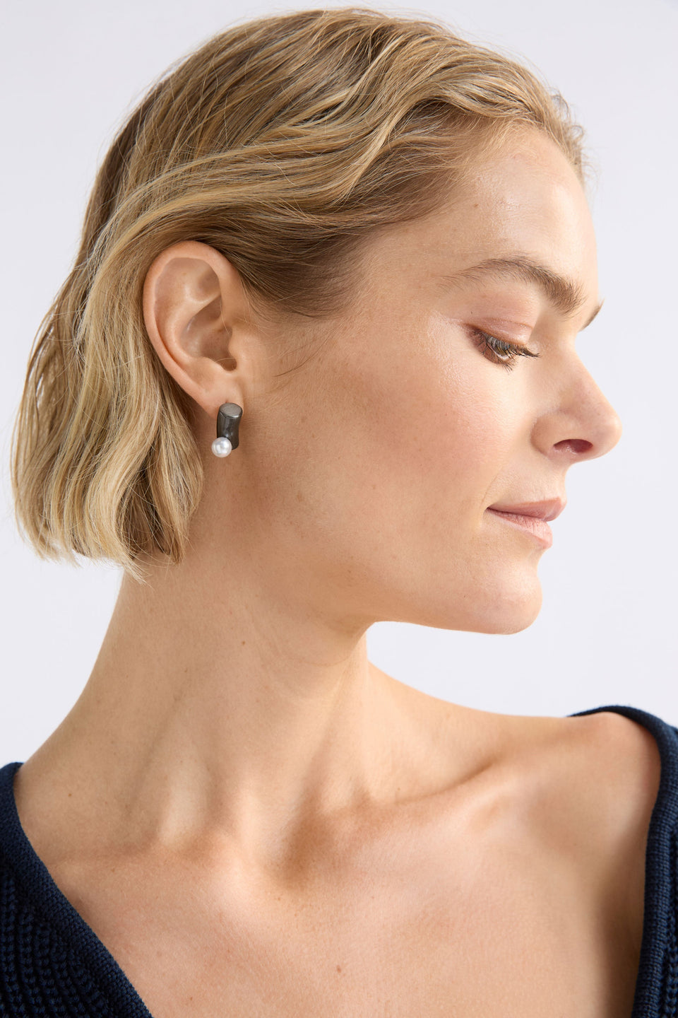 The Ahas Stud Earring features a sculptural curved form with a bold cylindrical base and delicate pearl bead accent on model close up | GUNMETAL