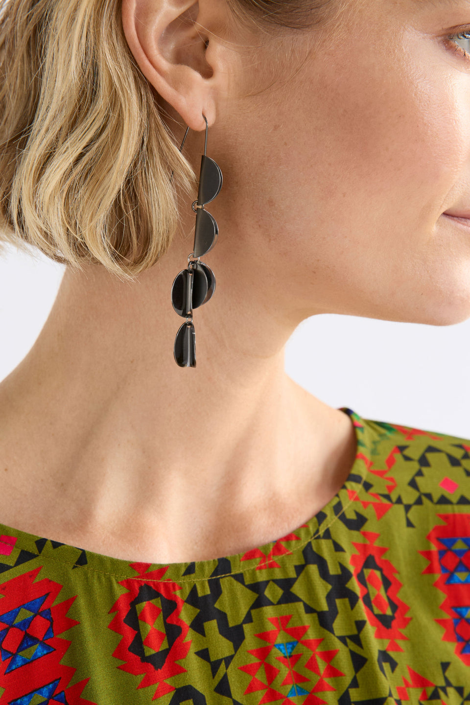 The Fossen Drop Earring features folded metal discs in a vertical row with a brushed finish on model ELK | GUNMETAL