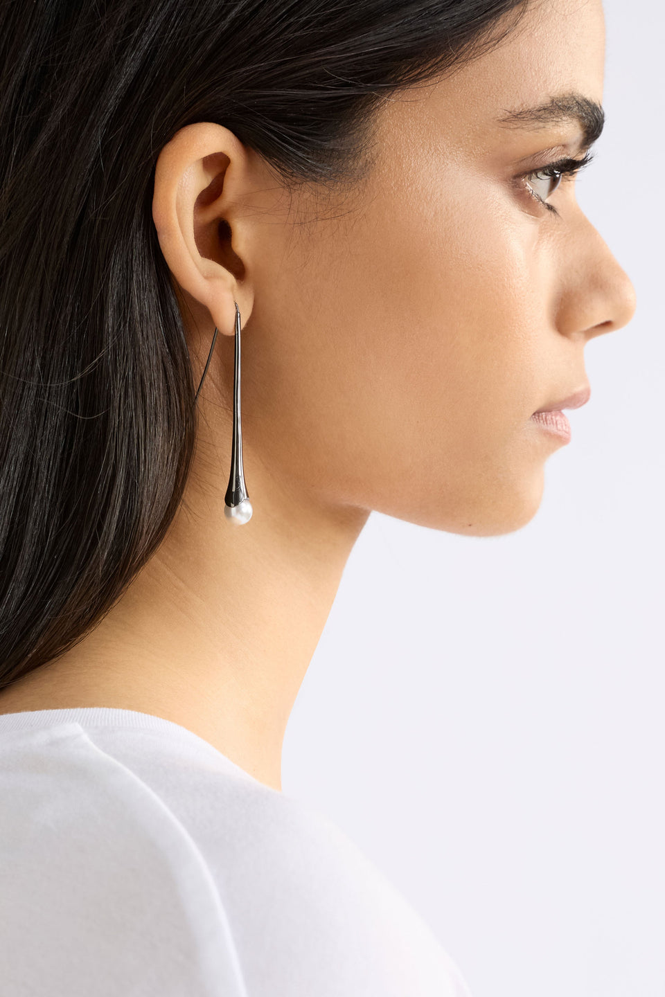 The Orbyn Drop Earring showcases an elongated stem with a faux pearl bead, offering a refined and elegant hook silhouette, shown on model | GUNMETAL