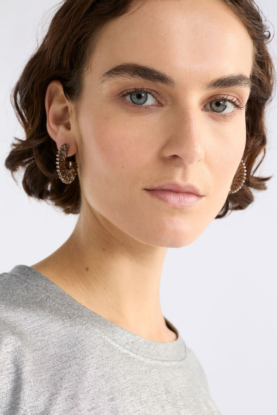 The Krusen Hoop Earring features a mid-sized open hoop crafted from shiny metal with a distinctive ridged texture on model ELK | GUNMETAL