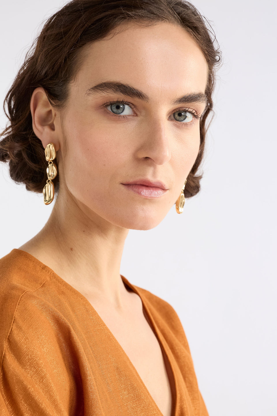 The Delaa Drop Earring features three sculptural rounded shapes linked for soft, organic movement on model ELK | GOLD