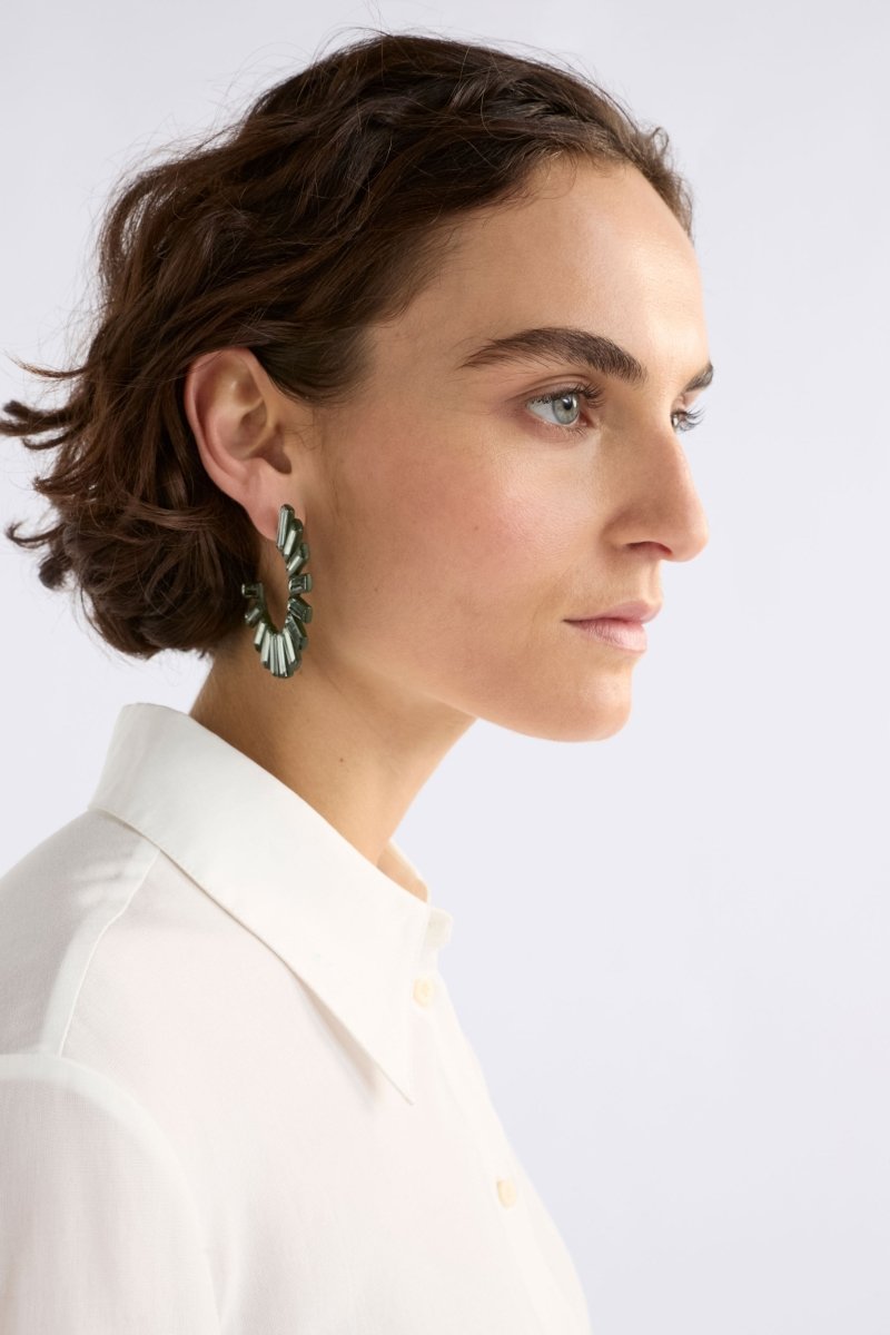 The Jule Large Hoop Earring features a circular fan of tonal glass beads radiating from a large hoop for a fun, glistening statement on model ELK | DARK OLIVE