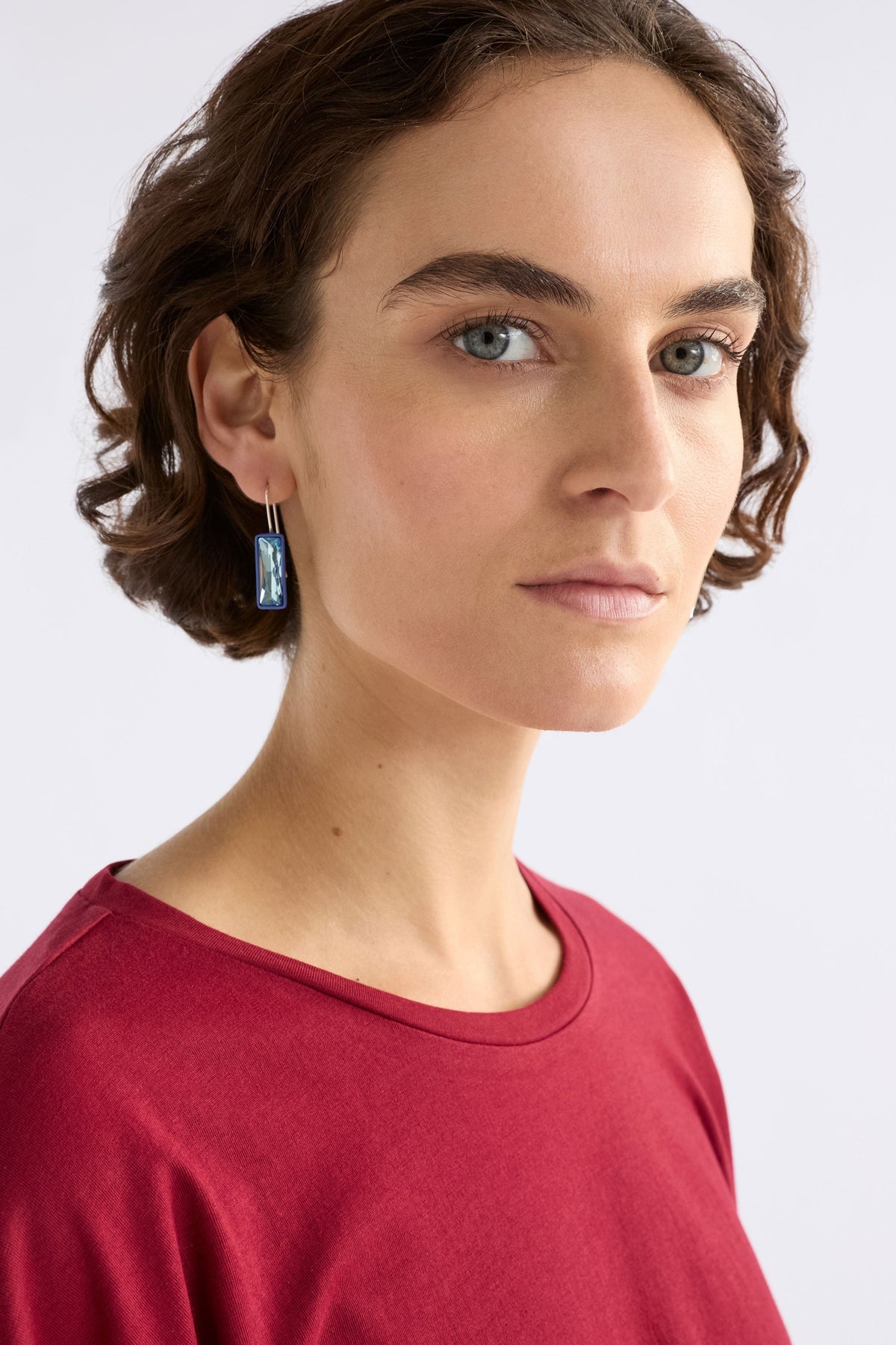 The Jule Small Hook Earring features a single glass stone with tonal rubberised casing and a simple hook, offering lightweight refinement, on model | BLUE MIST