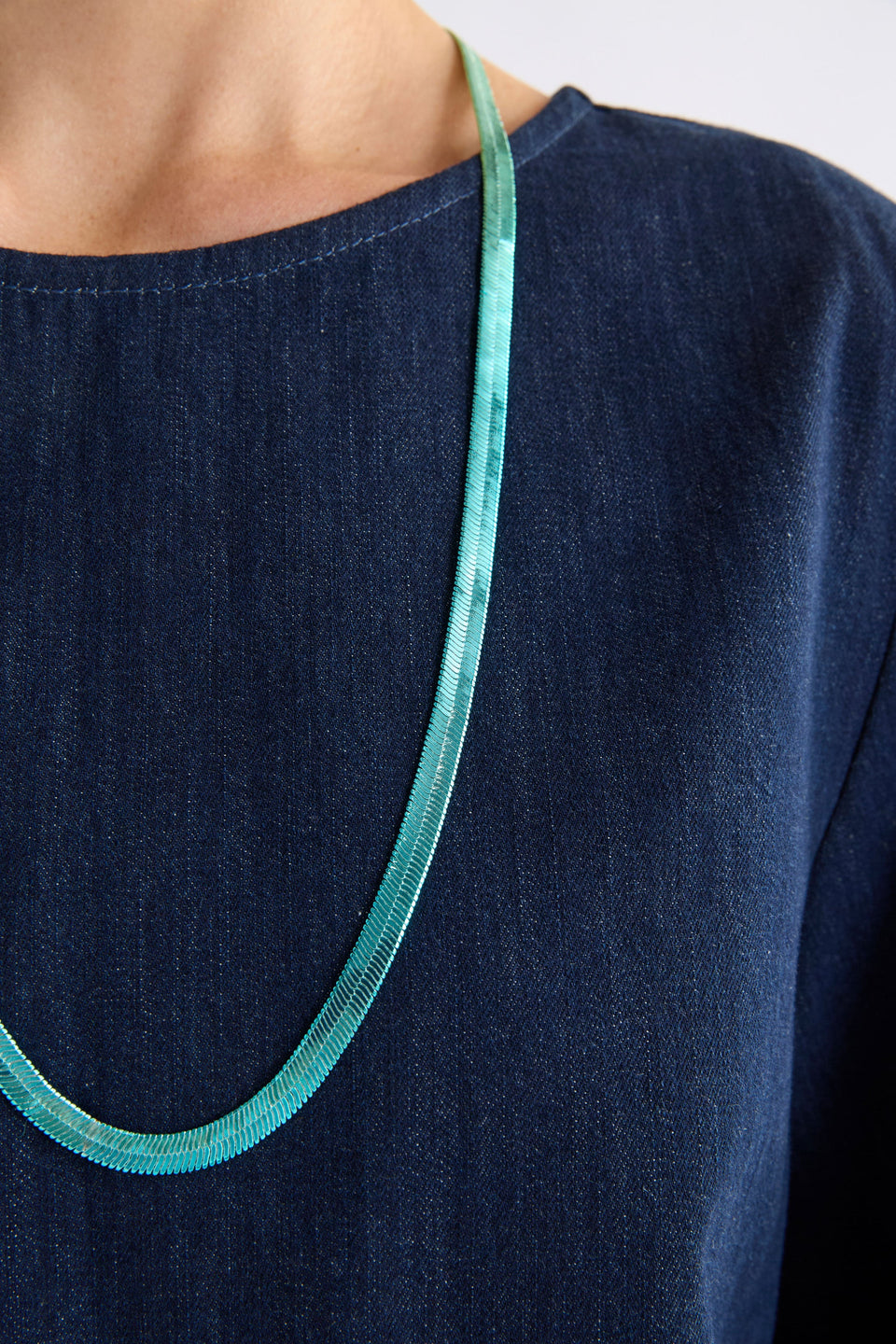 The Vera Long Necklace features a wide, flat snake chain in a shiny ombré finish, adding glistening colour and movement to any look on model ELK | GREEN-BLUE OMBRE