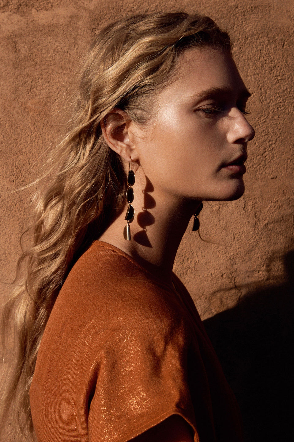 The Fossen Drop Earring features folded metal discs in a vertical row with a brushed finish on model ELK | GOLD