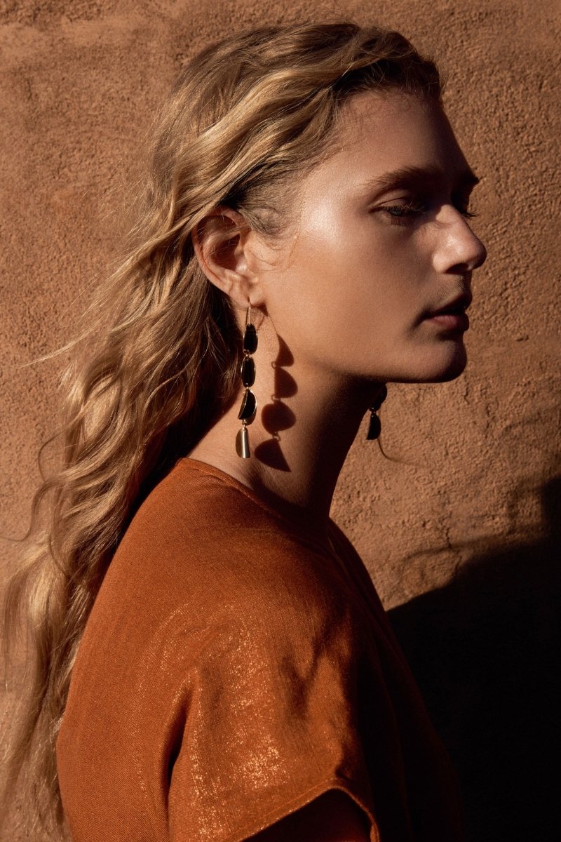 The Fossen Drop Earring features folded metal discs in a vertical row with a brushed finish on model ELK | GOLD
