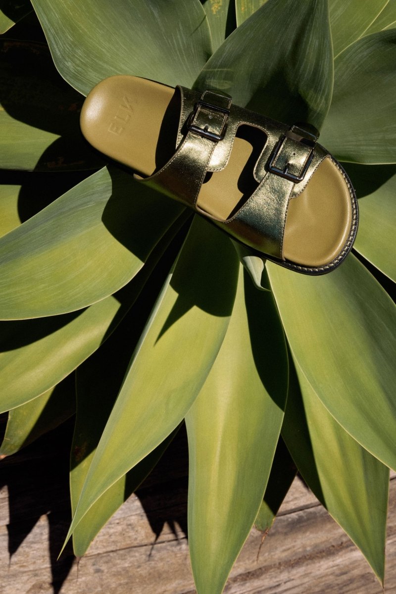The Spenne Sandal features dual buckled foiled leather straps with tonal western hardware in a metallic slide design ELK campaign | OLIVE