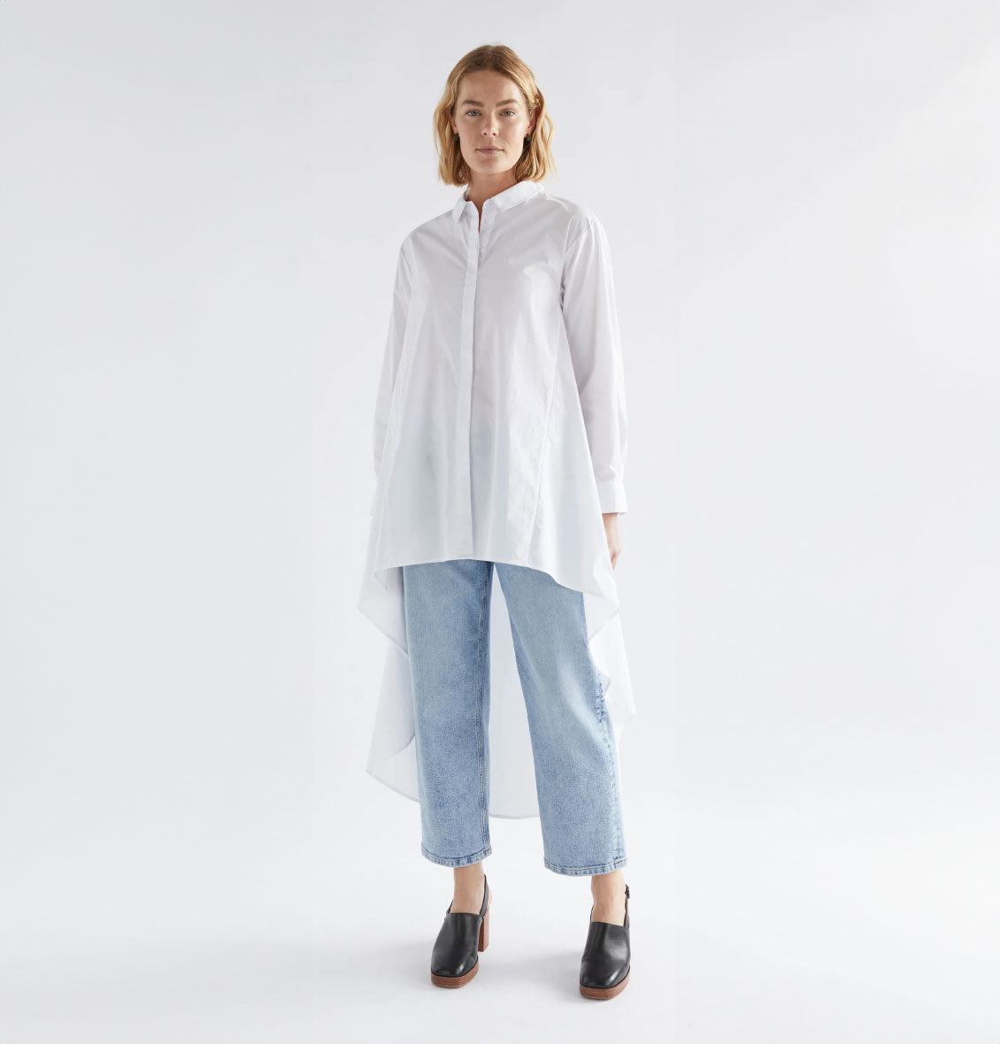 Model wearing Flikrin Shirt in crisp white with flowing hem, paired with light-wash denim jeans and black heeled shoes