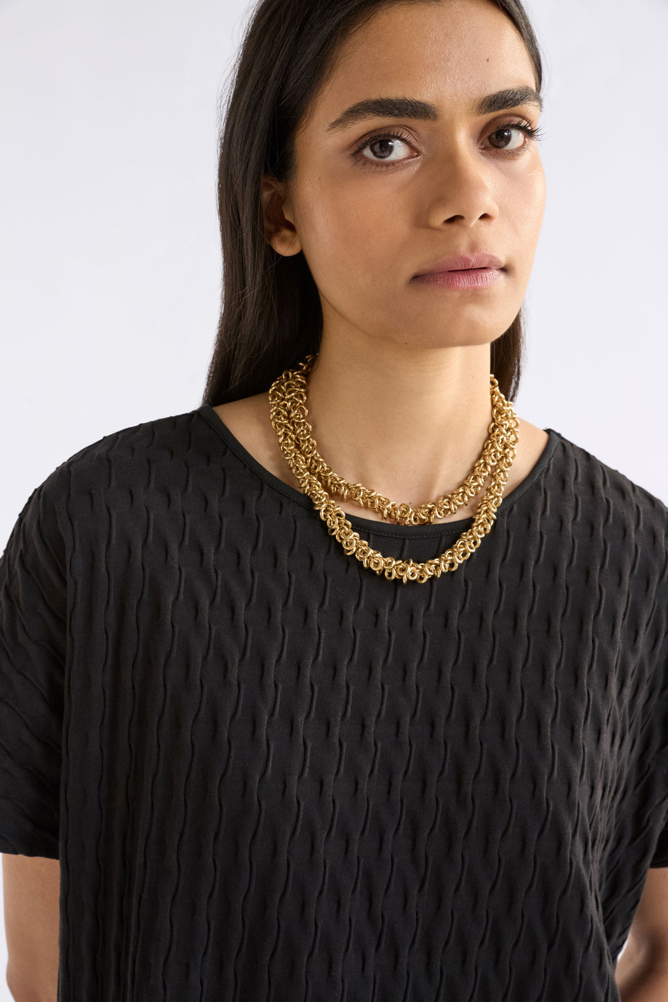 The Hava Necklace features layered metallic jump rings forming a thick, textured chain with sculptural impact on model ELK | GOLD